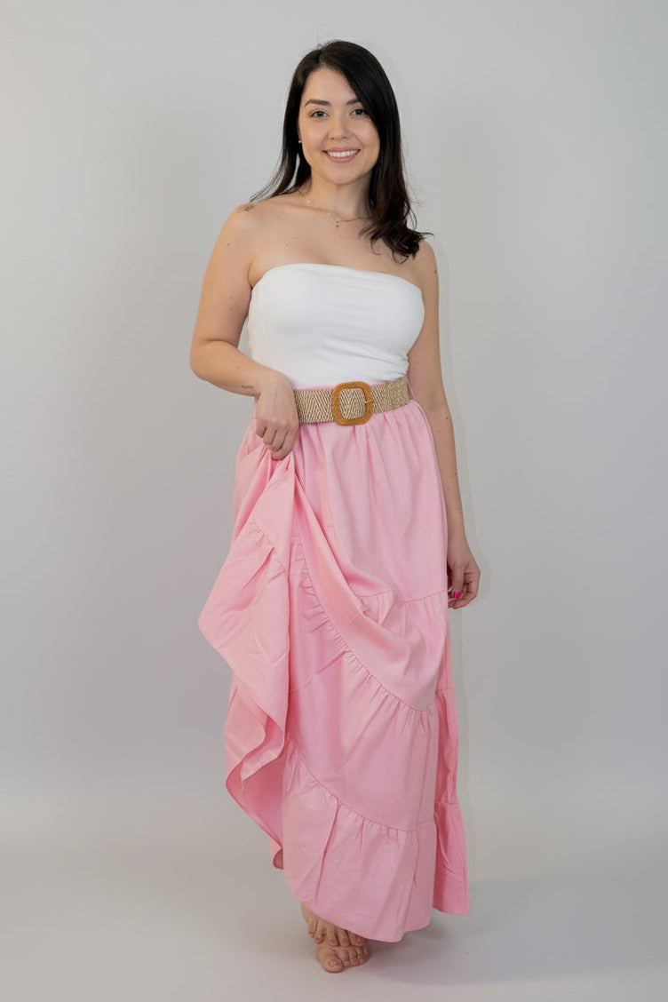 Woman wearing a white strapless top and pink ruffled skirt with a gold belt against a white background