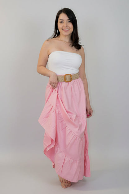Woman wearing a white strapless top and pink ruffled skirt with a gold belt against a white background