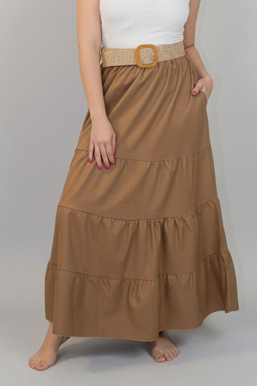 Woman wearing a white strapless top and brown tiered skirt with a belt against a white background