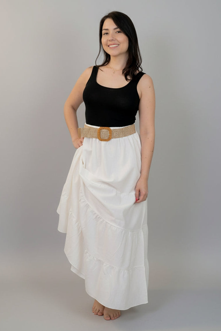 Woman wearing a black top and white skirt with a gold belt against a white background