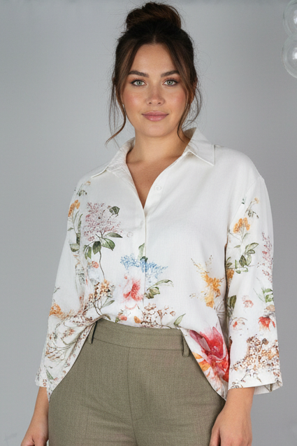 Woman wearing a floral blouse and beige pants against a plain background